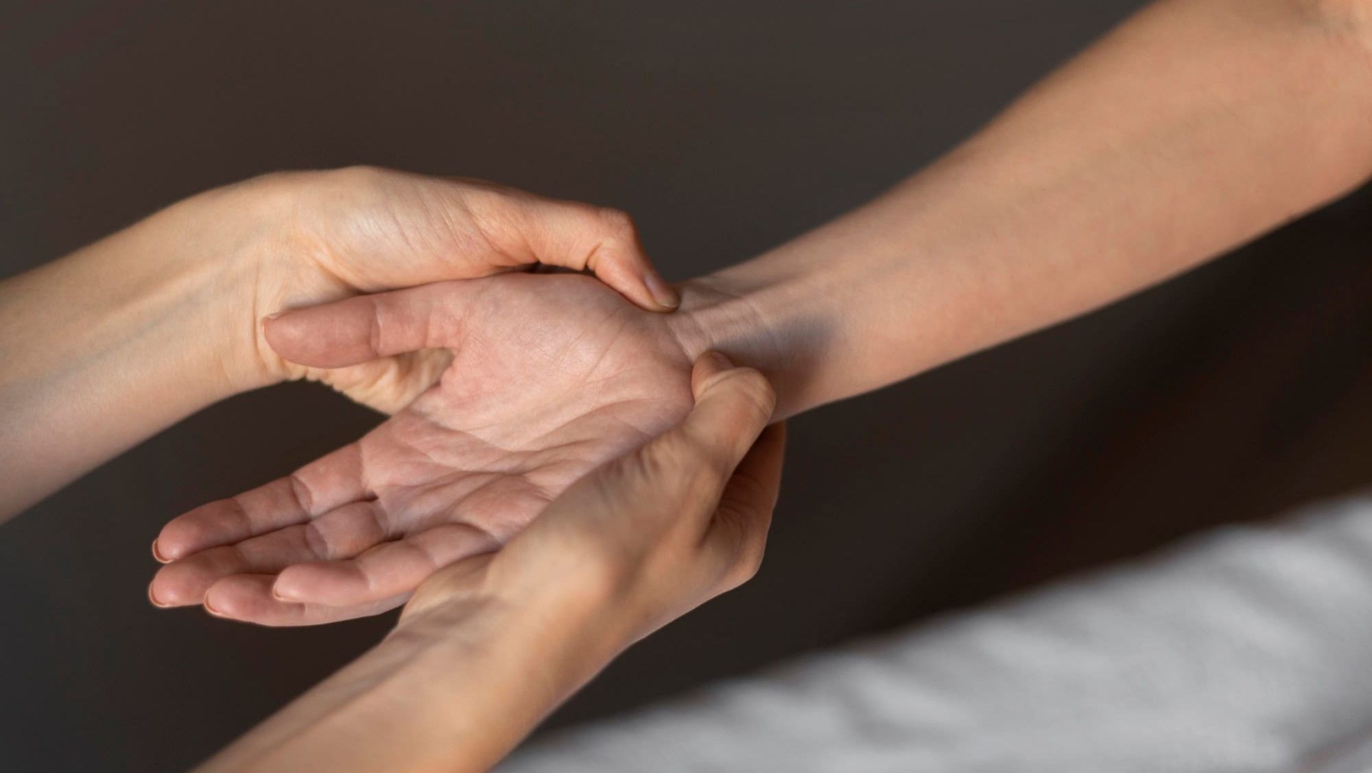 Nærbilde av hender hvor en person trykker på håndleddet til en annen under behandling.